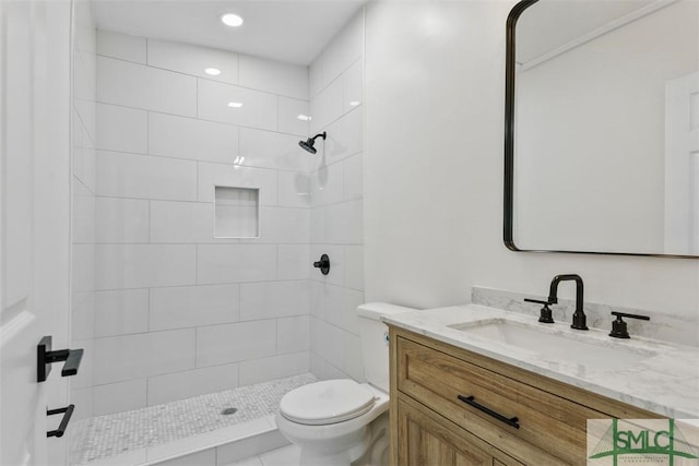 bathroom with a tile shower, vanity, and toilet