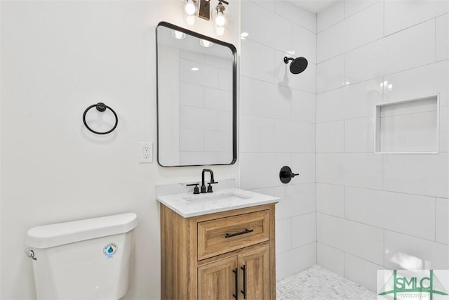 bathroom with toilet, tiled shower, and vanity