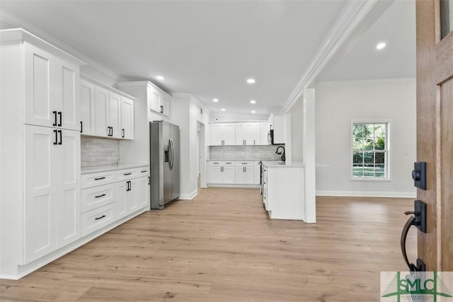 kitchen featuring light countertops, ornamental molding, white cabinetry, light wood-type flooring, and stainless steel fridge