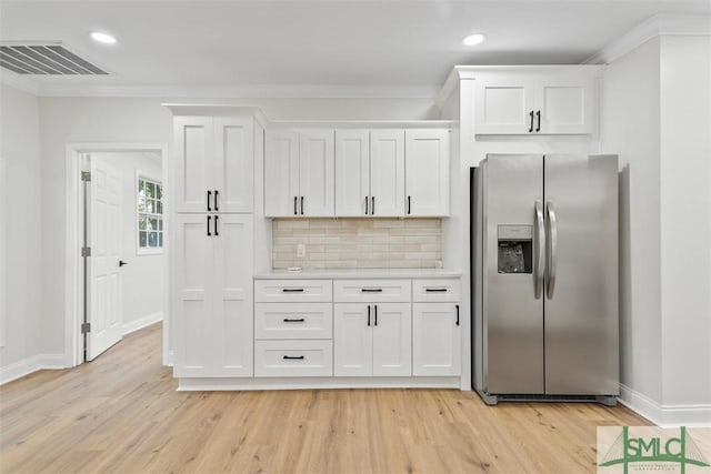 kitchen featuring visible vents, white cabinets, ornamental molding, backsplash, and stainless steel fridge