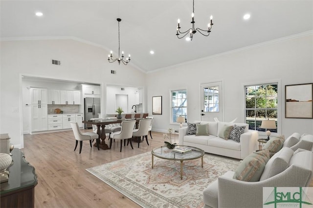 living area featuring high vaulted ceiling, a notable chandelier, visible vents, light wood-style floors, and crown molding