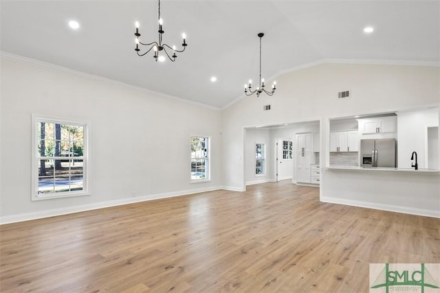 unfurnished living room with crown molding, light wood finished floors, visible vents, an inviting chandelier, and a sink