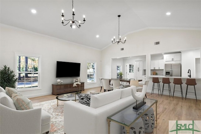 living area featuring visible vents, baseboards, light wood-style flooring, ornamental molding, and a chandelier