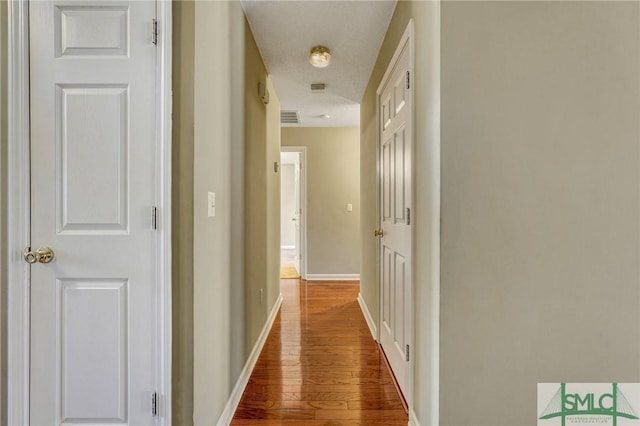 hall with visible vents, baseboards, and wood finished floors