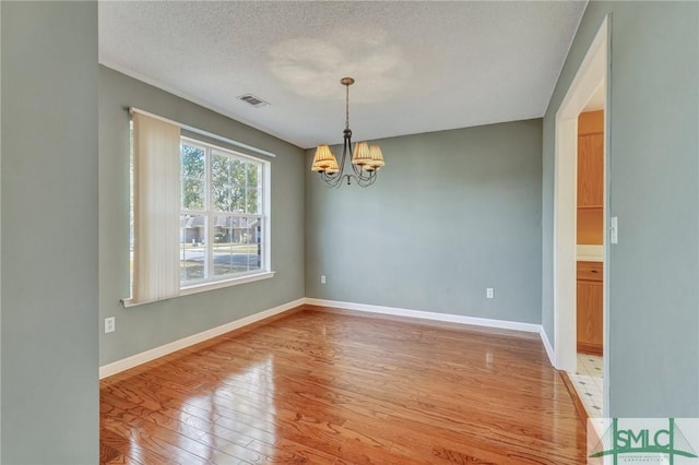 spare room with baseboards, visible vents, an inviting chandelier, a textured ceiling, and light wood-style floors