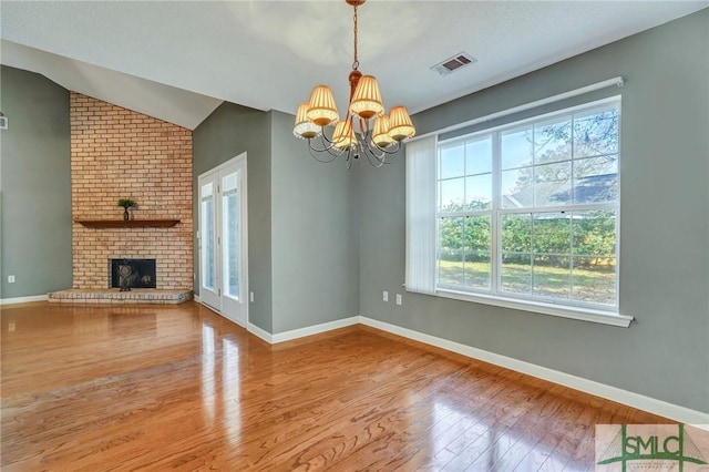 unfurnished living room featuring lofted ceiling, visible vents, a brick fireplace, wood finished floors, and baseboards