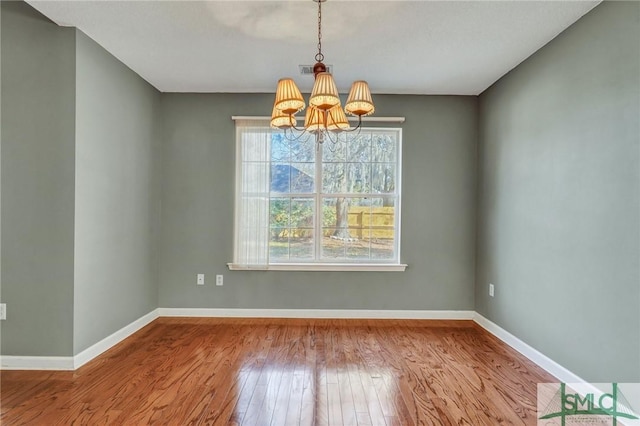 unfurnished dining area with visible vents, an inviting chandelier, hardwood / wood-style flooring, and baseboards