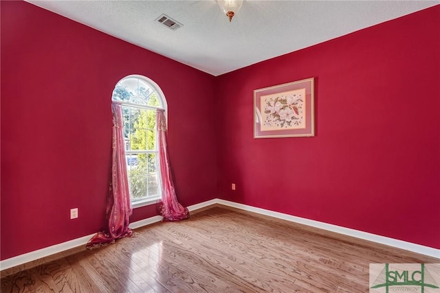 unfurnished room featuring baseboards, a textured ceiling, visible vents, and wood finished floors