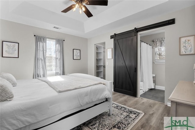 bedroom featuring a barn door, visible vents, baseboards, a tray ceiling, and light wood-type flooring