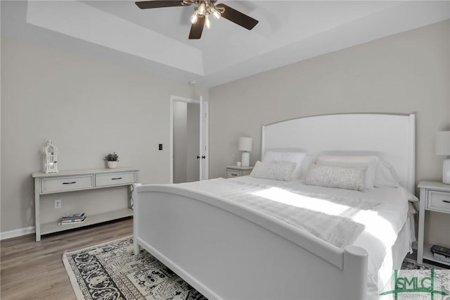 bedroom with light wood finished floors, baseboards, a raised ceiling, and a ceiling fan