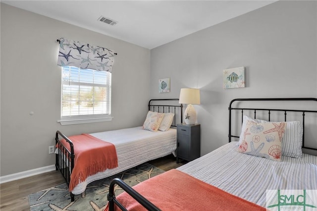 bedroom with baseboards, visible vents, and wood finished floors