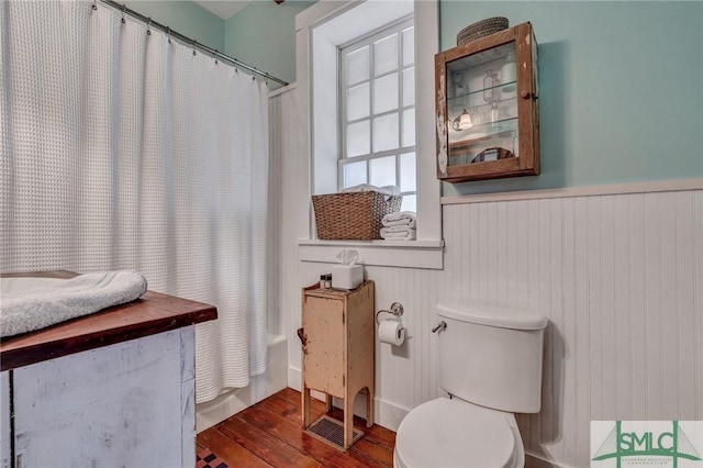 full bathroom with shower / bath combo with shower curtain, wainscoting, toilet, and wood finished floors