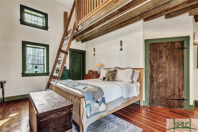 bedroom featuring a towering ceiling, wood finished floors, beam ceiling, and baseboards