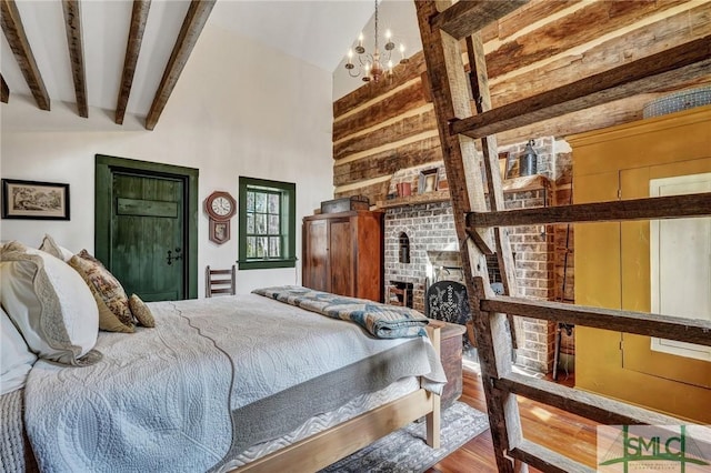 bedroom with wood finished floors, an inviting chandelier, wood walls, a fireplace, and beam ceiling