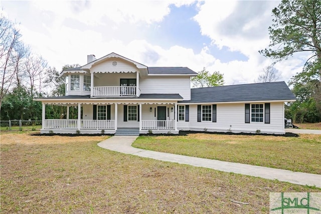 view of front of property featuring covered porch, a front lawn, a chimney, and a balcony