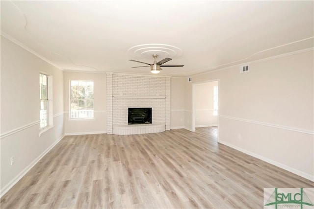 unfurnished living room with ceiling fan, a brick fireplace, visible vents, and crown molding