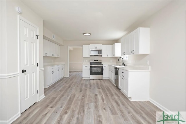 kitchen featuring light wood-style floors, appliances with stainless steel finishes, white cabinets, and a sink