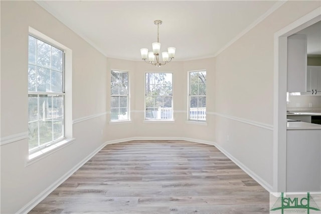 unfurnished dining area featuring light wood-style floors, a chandelier, crown molding, and baseboards