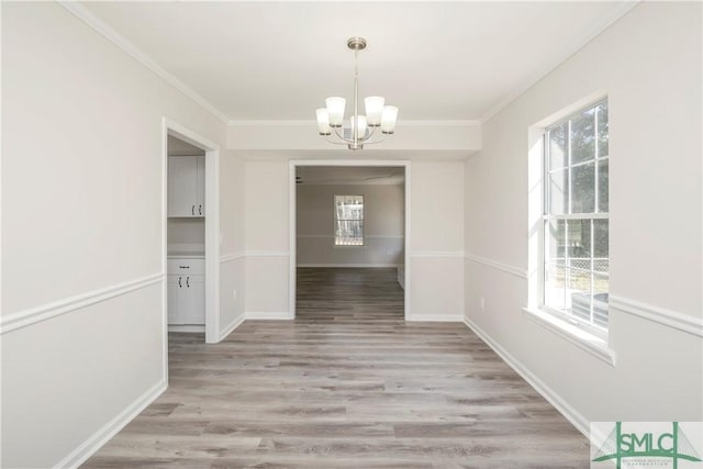 unfurnished dining area with a healthy amount of sunlight, light wood-style flooring, a chandelier, and ornamental molding