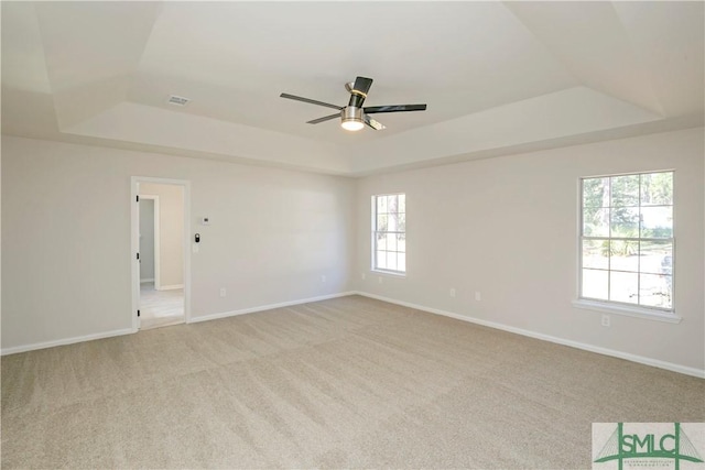 unfurnished room featuring a raised ceiling, light colored carpet, and baseboards