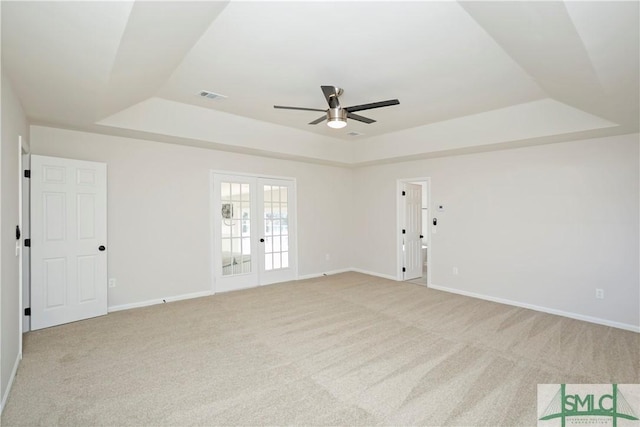 unfurnished room with light carpet, visible vents, baseboards, french doors, and a raised ceiling