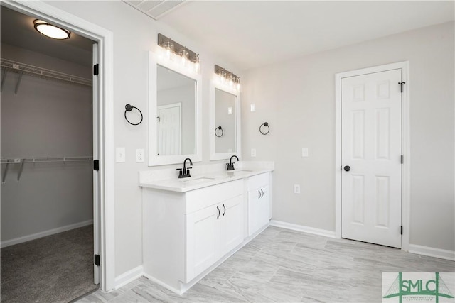 full bath featuring a walk in closet, a sink, baseboards, and double vanity