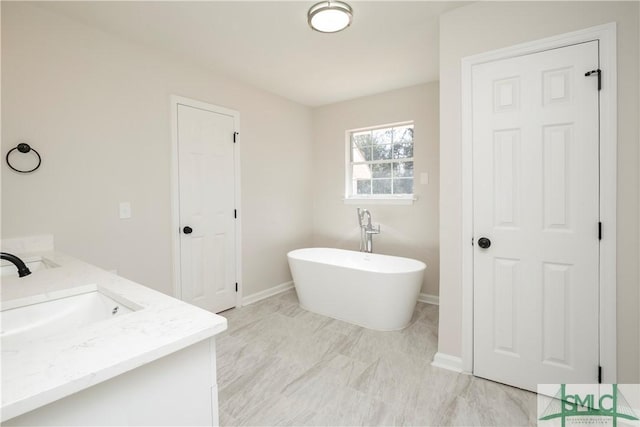 full bathroom featuring a freestanding bath, double vanity, a sink, and baseboards