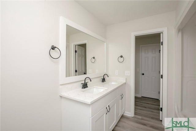 bathroom featuring double vanity, wood finished floors, a sink, and baseboards