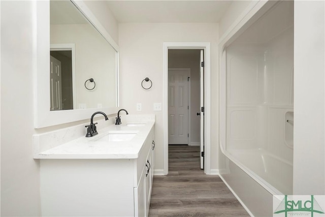 full bath featuring double vanity, a sink, shower / tub combination, wood finished floors, and baseboards