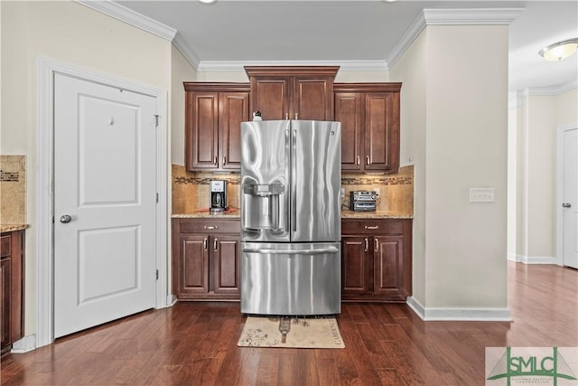 kitchen with light stone countertops, stainless steel fridge, ornamental molding, and dark wood finished floors