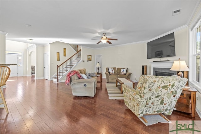 living area featuring a fireplace, visible vents, stairs, ornamental molding, and dark wood-style floors