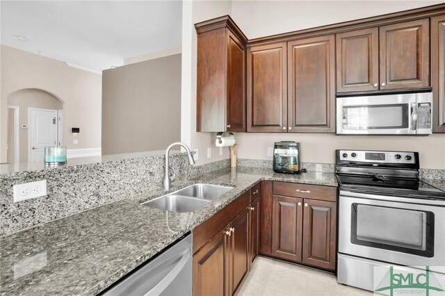 kitchen with arched walkways, stone counters, light tile patterned flooring, a sink, and appliances with stainless steel finishes