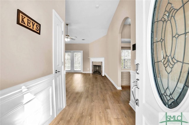 entryway with light wood-style floors, ceiling fan, arched walkways, and a tile fireplace