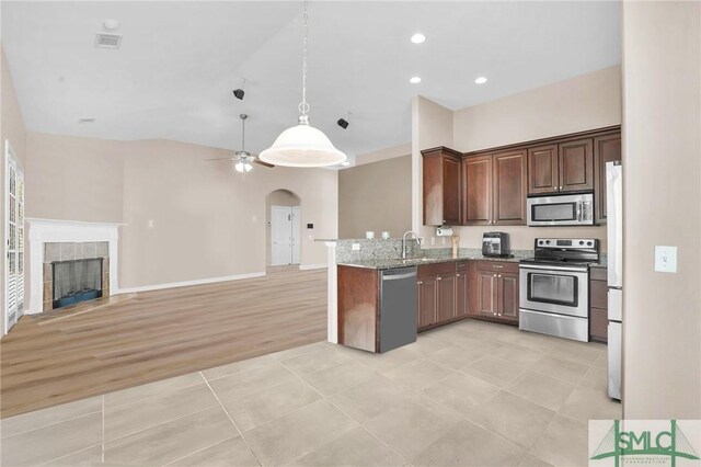 kitchen featuring light stone counters, arched walkways, appliances with stainless steel finishes, open floor plan, and a tile fireplace