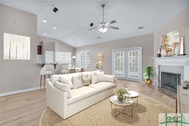 living area with lofted ceiling, recessed lighting, a fireplace with flush hearth, visible vents, and light wood finished floors