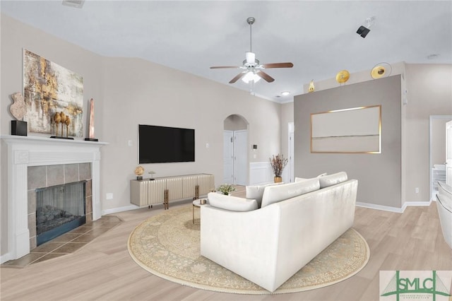 living room with arched walkways, a fireplace, ceiling fan, wood finished floors, and baseboards