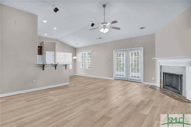 unfurnished living room with lofted ceiling, visible vents, baseboards, light wood finished floors, and a tiled fireplace