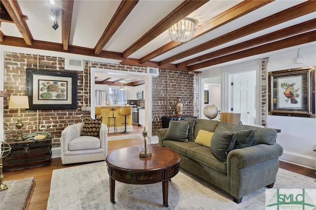 living area with beamed ceiling, brick wall, and wood finished floors