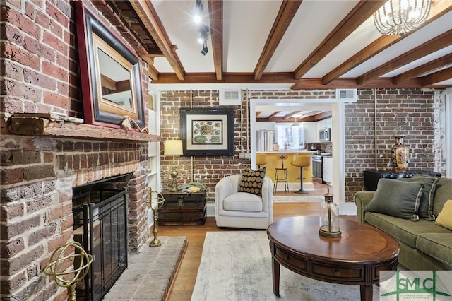 living area with visible vents, brick wall, light wood-style flooring, beamed ceiling, and a brick fireplace