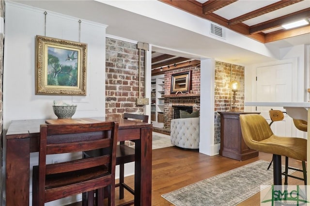 dining space featuring visible vents, brick wall, wood finished floors, a brick fireplace, and beam ceiling