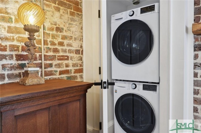 washroom featuring stacked washer and clothes dryer, brick wall, and laundry area