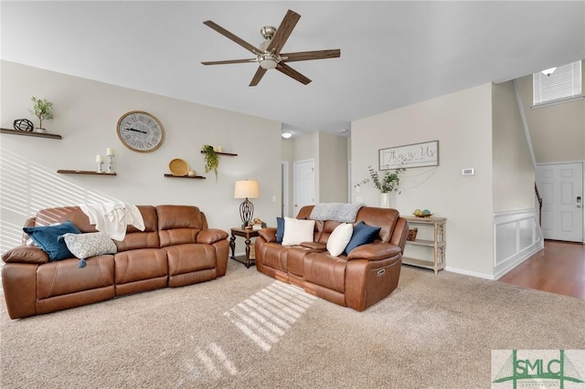 living area featuring a wainscoted wall, carpet floors, a ceiling fan, and a decorative wall