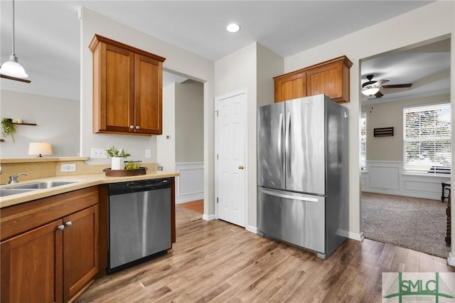 kitchen with a sink, light countertops, appliances with stainless steel finishes, wainscoting, and brown cabinetry