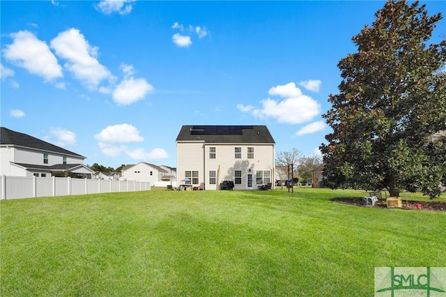 rear view of house with a yard, solar panels, and fence