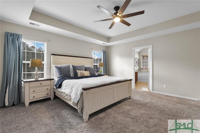 carpeted bedroom with connected bathroom, a raised ceiling, visible vents, and baseboards