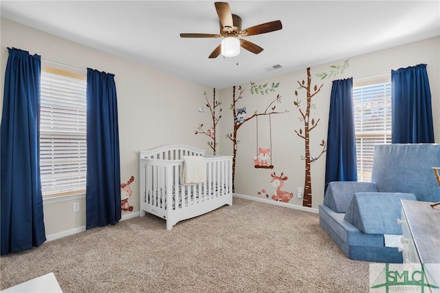 carpeted bedroom featuring a nursery area, visible vents, ceiling fan, and baseboards