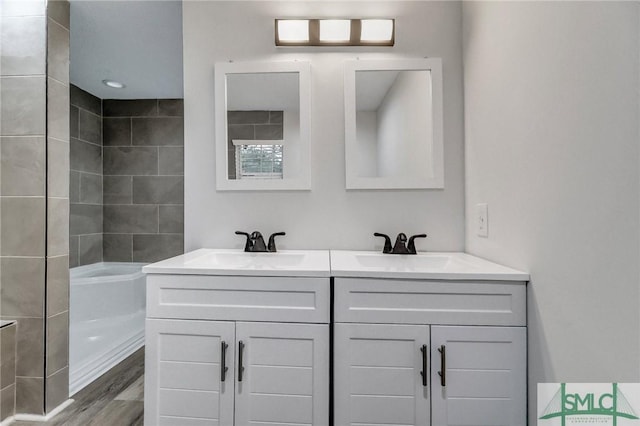 full bathroom with wood finished floors, a sink, a bathing tub, and double vanity