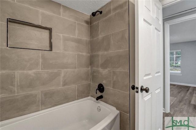 bathroom with a textured ceiling, baseboards, wood finished floors, and shower / bathing tub combination