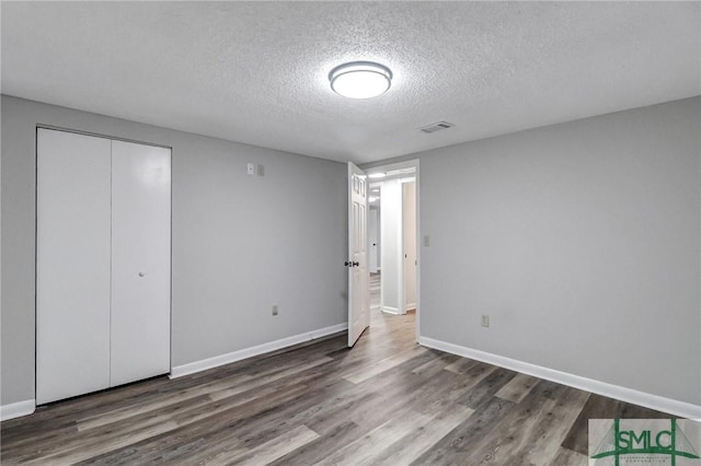 unfurnished bedroom with a textured ceiling, wood finished floors, visible vents, baseboards, and a closet