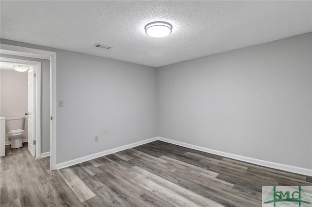 interior space with visible vents, a textured ceiling, baseboards, and wood finished floors